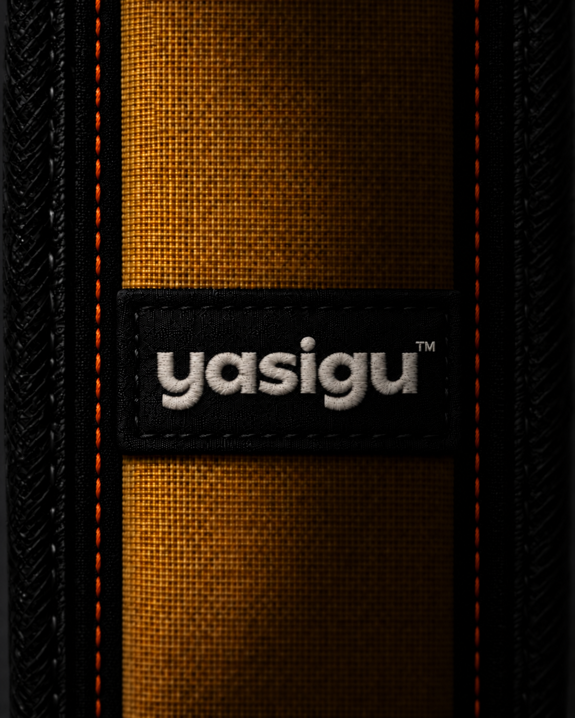 Shadowed concept detail of the YASIGU shoulder pad with fine orange stitching on the black structural facings and white embroidered YASIGU™ lettering.